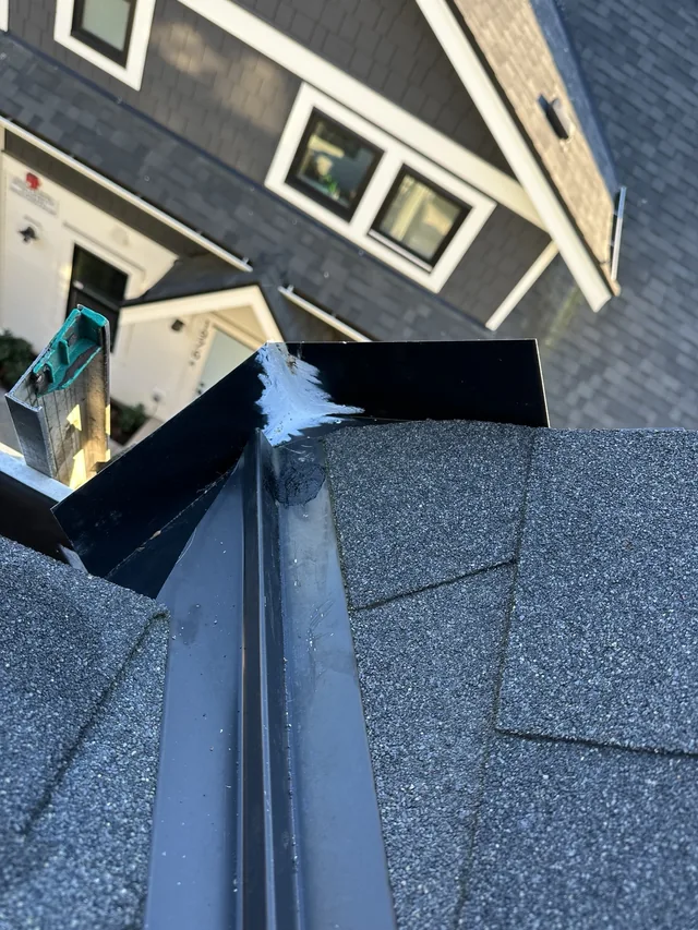 Metal diverter at the end of a roof valley, with sealant visible at the corner.