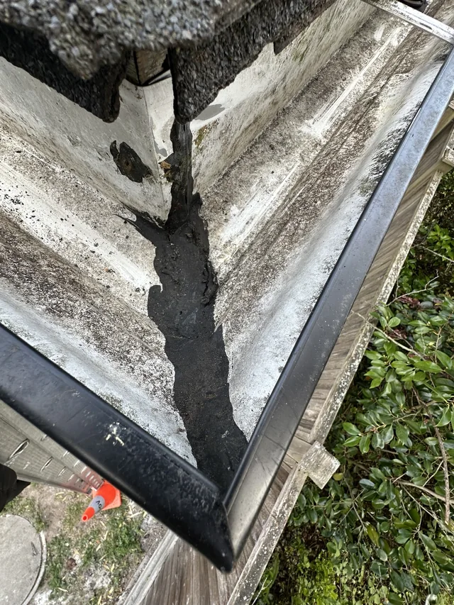 Gutter corner with old dark sealant before resealing.