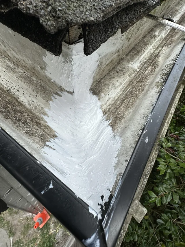 The same gutter corner with white sealant applied along the seam.